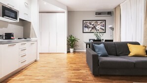 Een moderne keuken met witte kasten en een ingebouwde magnetron. Er is een zithoek met een grijze bank en een potplant.