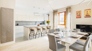Eine moderne Küche mit weißen Schränken, einer zentralen Kochinsel mit Barhocker und einem Essbereich mit Tisch für vier Personen.