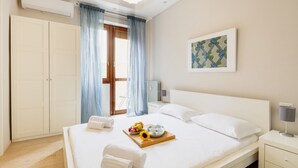 Ein Hotelzimmer mit einem großen Bett, einem Nachttisch mit Lampe, einem gerahmten Kunstwerk an der Wand und einem Fenster mit Vorhängen.