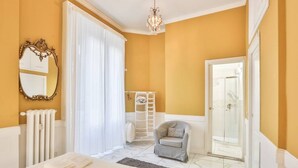 Ein Schlafzimmer mit einem Bett, einem Stuhl, einem Heizkörper, einem Spiegel und einer Tür zu einem Badezimmer.