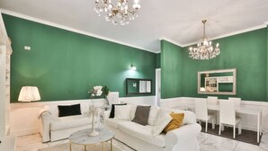 Ein Wohnzimmer mit grüner Wand, weißen Möbeln, einer Chandelier und einem Essbereich.
