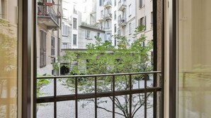 Blick durch ein Fenster mit Metallgitter auf eine Kopfsteinpflasterstraße, im Hintergrund sind Gebäude zu sehen.