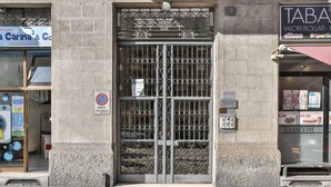 Ein schmiedeeisernes Tor mit aufwendigen Verzierungen, ein Verbotsschild für Parkplätze und ein Ladenlokal mit einem Schild für 'Tabacco'.