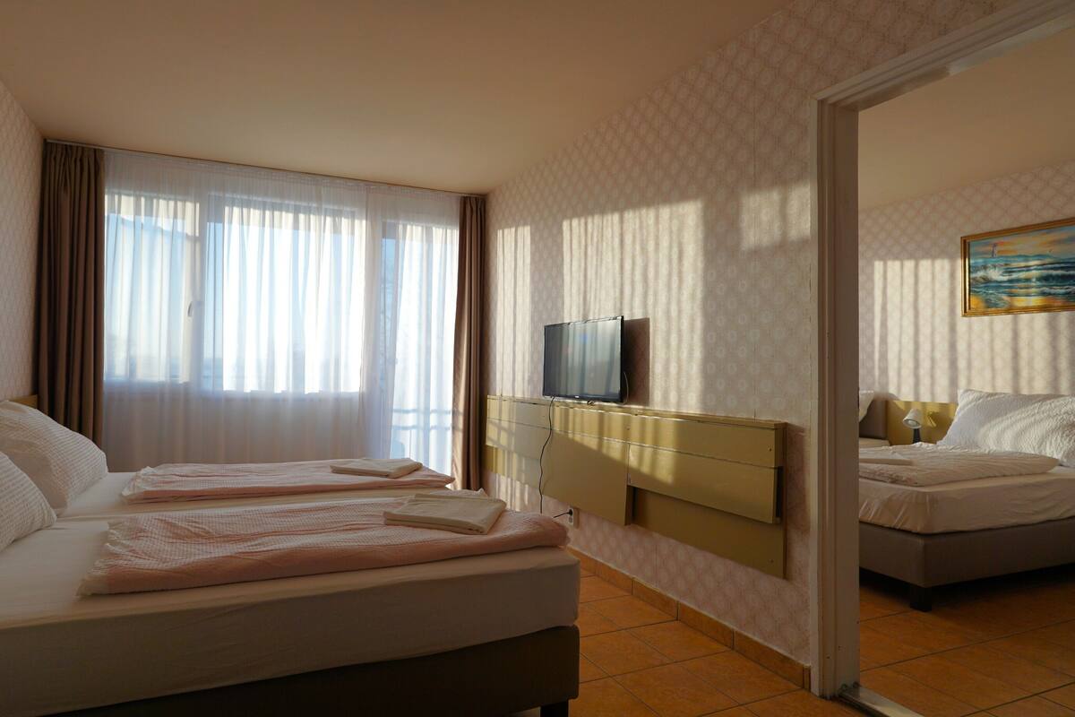A hotel room with two beds, a television on a dresser, and a painting on the wall.