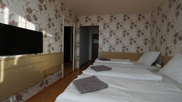 Habitación de hotel con televisor sobre una cómoda, dos camas con sábanas blancas y un estampado de flores en el papel tapiz.