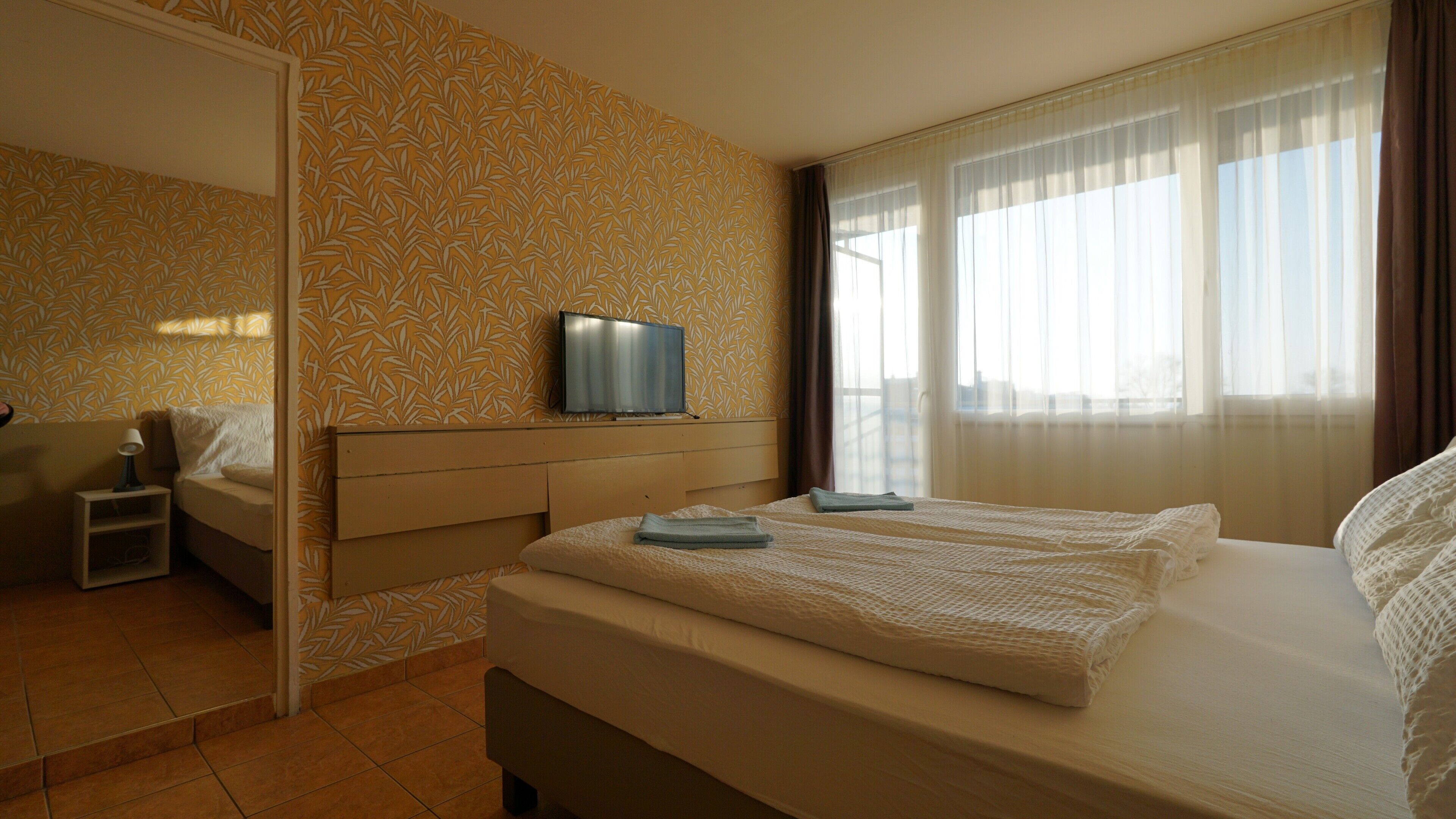 A hotel room with a bed, a TV on a stand, a nightstand, and a window with curtains.