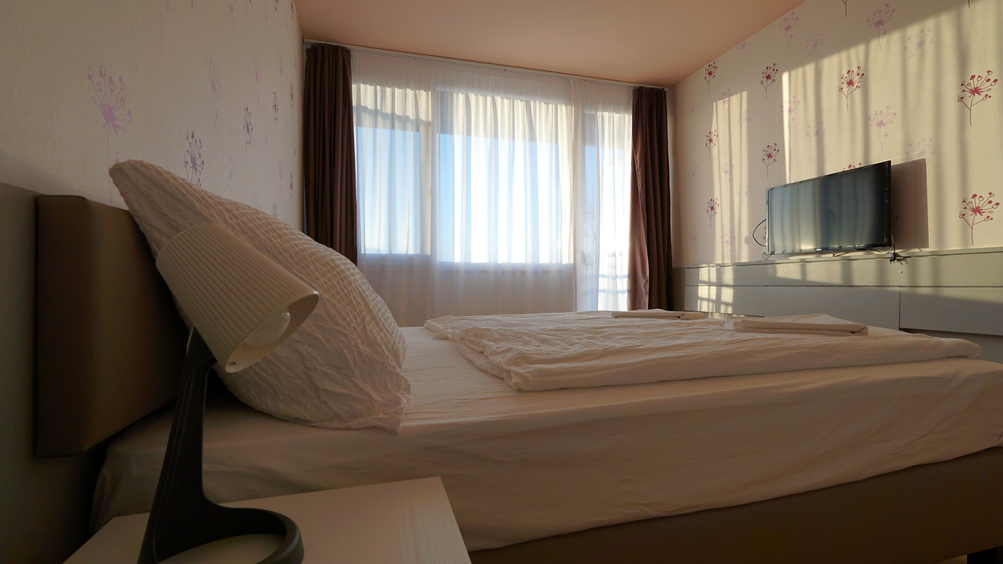 Une chambre d’hôtel avec un lit, un téléviseur fixé au mur et une fenêtre avec des rideaux.