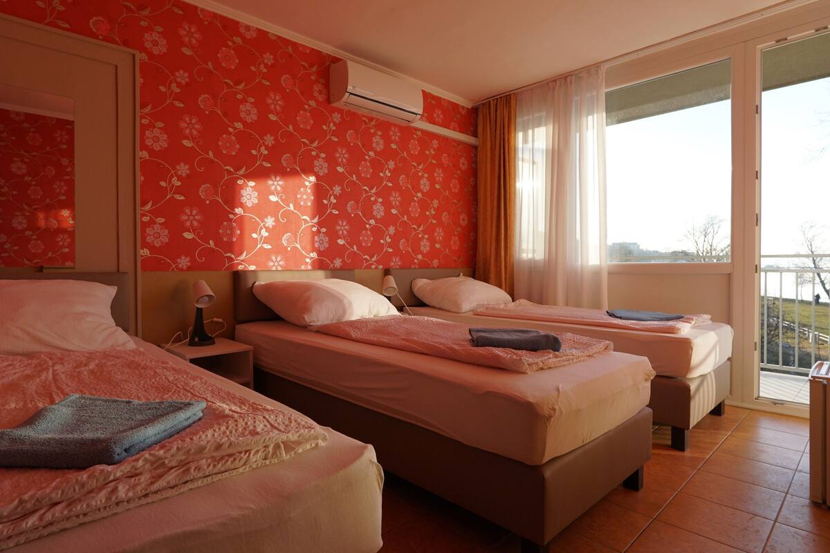 A hotel room with two beds, a window with a view, and an air conditioning unit.