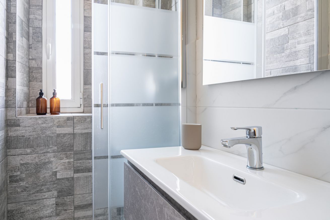 Une salle de bain moderne avec un lavabo blanc, une cabine de douche en verre et un mur recouvert de carreaux en pierre.