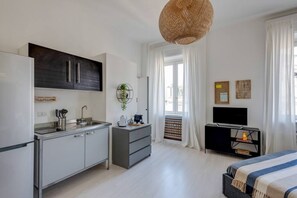 Una cocina moderna con refrigerador empotrado, un lavamanos y una cafetera. Hay un comedor con mesa y sillas, y un ventanal con cortinas.