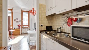 Une cuisine moderne avec des armoires blanches, un évier en acier inoxydable et un four à micro-ondes. Un lustre rouge est suspendu au-dessus du comptoir.