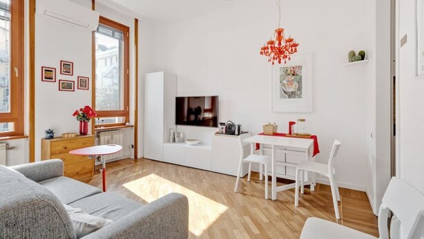 Un salon moderne avec un canapé, une table à manger et des chaises, un téléviseur et un lustre rouge.