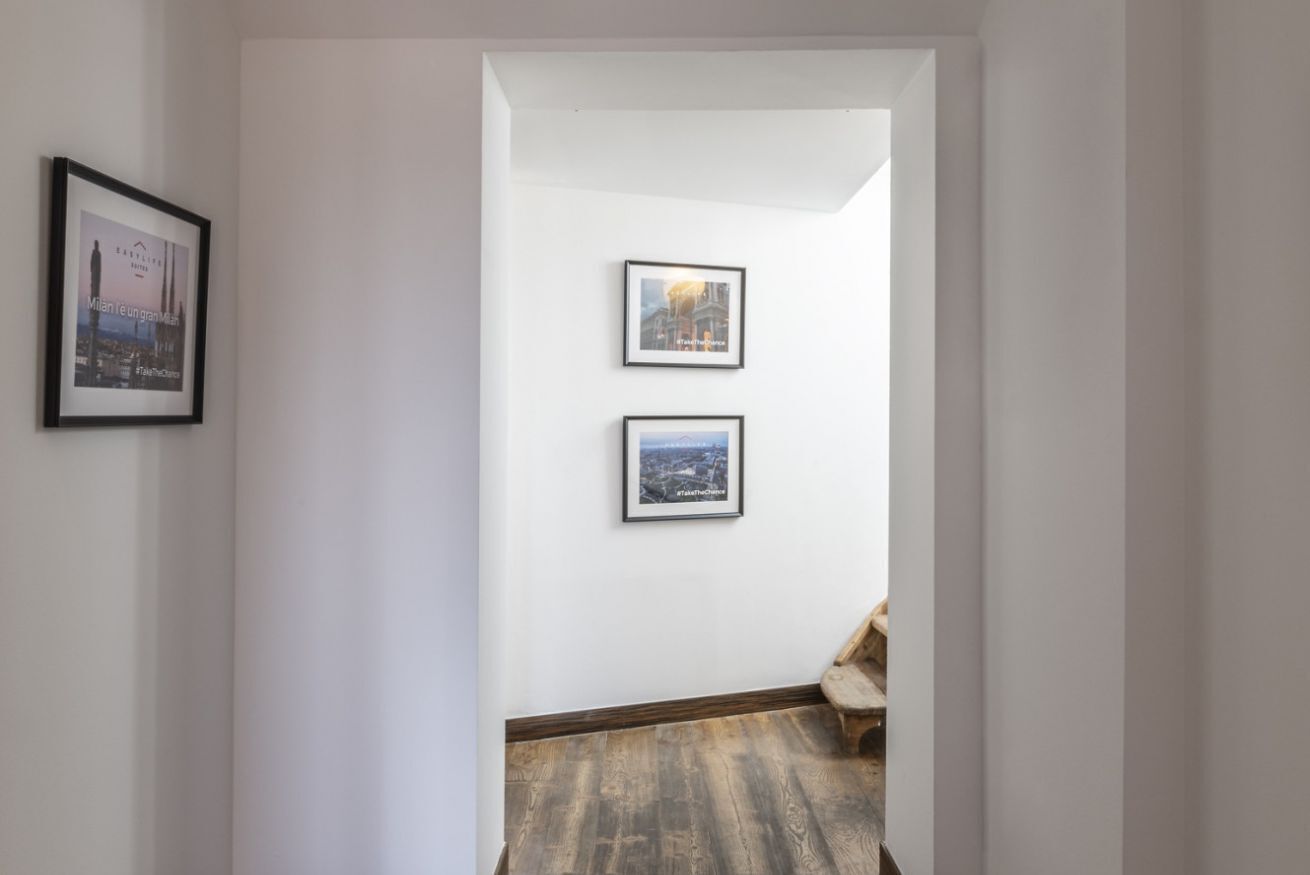 A hallway with a wooden floor and two framed pictures on the wall.
