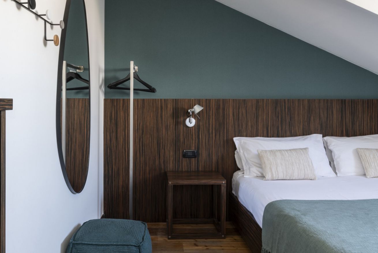 Een slaapkamer met een houten hoofdbord, een nachtkastje, een hanglamp en een spiegel.