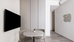 Un espace repas moderne avec une table ronde, deux chaises, une plante en pot et un téléviseur à écran plat fixé au mur.