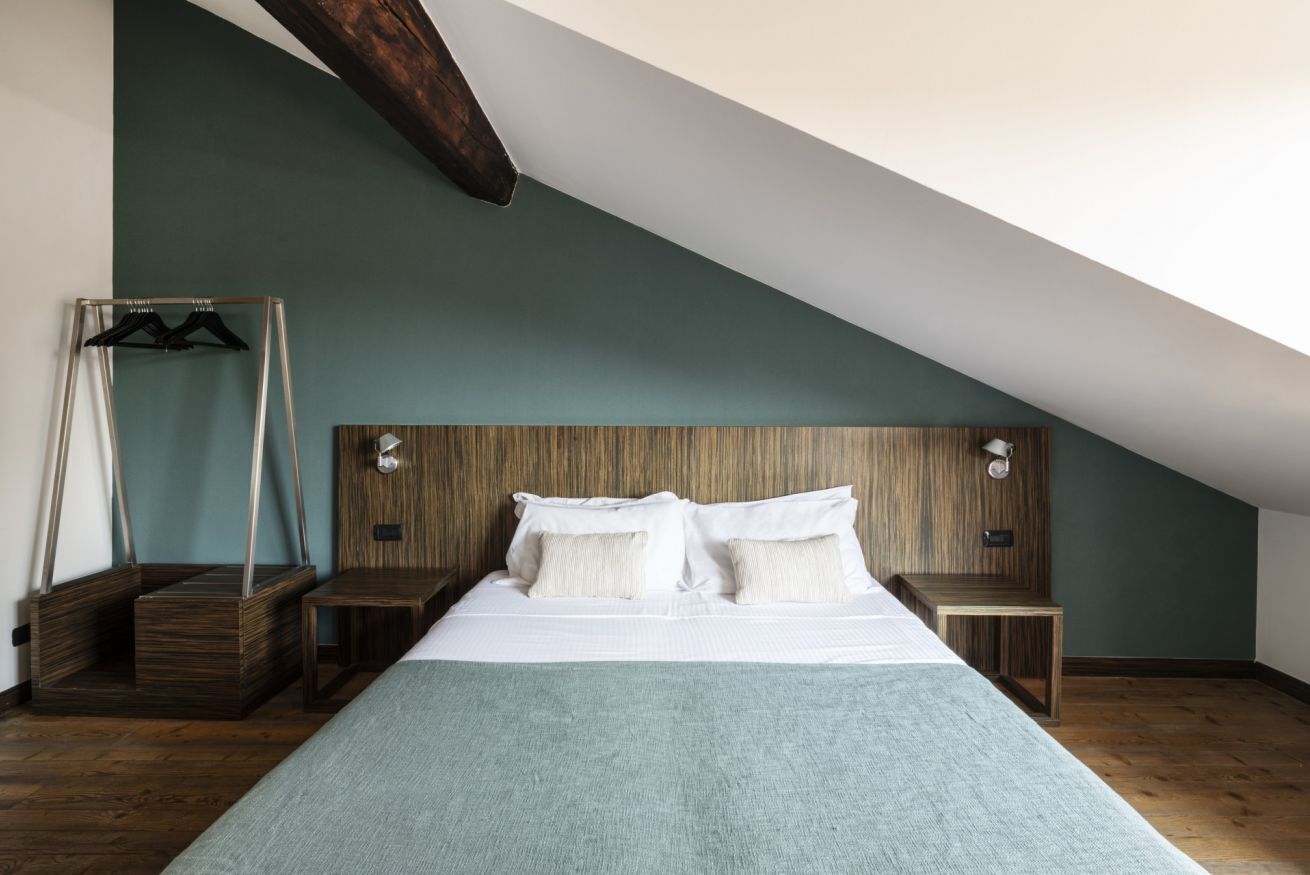 A bedroom with a sloped ceiling, a wooden headboard, a bed with white linens, a bedside table, and a hanging garment rack.