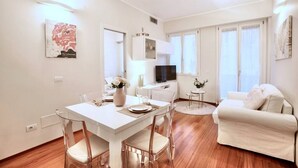 Ein modernes Wohnzimmer mit einem weißen Sofa, einem Esstisch mit Stühlen, einem Fernseher und Kunstwerken an den Wänden.