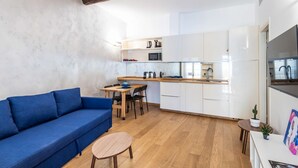 A modern living room with a blue sofa, wooden dining table, and a kitchen area with white cabinets and a wooden countertop. - Easylife - Romantic flat in Darsena (Navigli) (Milano)