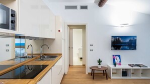 A modern kitchen with a wooden countertop, stainless steel sink, and built-in appliances. There is a dining area with a small table and chairs, and a white console table with decorative items. - Easylife - Romantic flat in Darsena (Navigli) (Milano)
