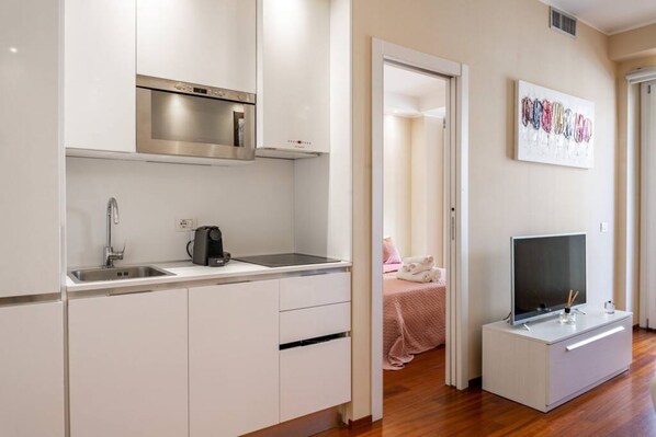 A compact kitchen with a built-in oven, a coffee maker, and a TV on a stand.