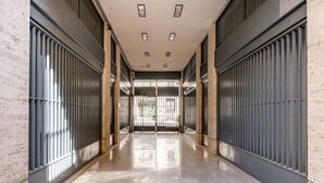 Um corredor com chão de mármore brilhante, grades de metal e uma porta de vidro no final.