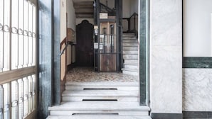Una escalera de mármol que conduce a una puerta de madera oscura, con una reja metálica a la izquierda y un piso de baldosas.