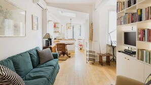A spacious living room with a teal sofa, a bookshelf, and a dining area with a table and chairs. - Easylife - Comfortable studio with terrace Navigli (Milano)