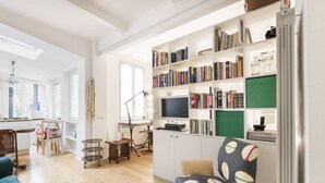 A spacious living room with a large bookshelf, a comfortable armchair, and a television. - Easylife - Comfortable studio with terrace Navigli (Milano)