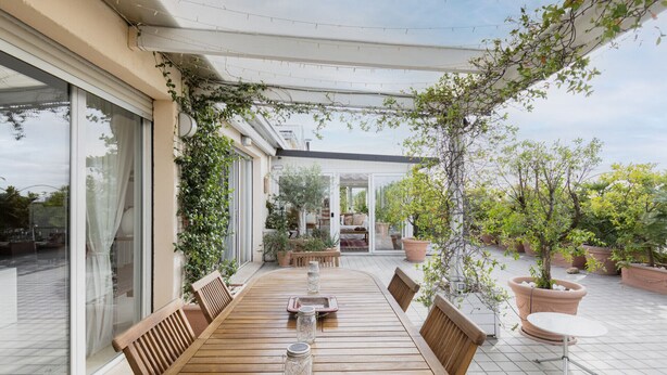 A covered patio with a wooden table and chairs, surrounded by potted plants and a view of the interior. - Easylife - 230sqm attic with terrace Bocconi area (Milano)
