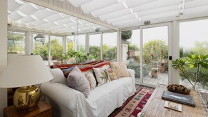 A sunroom with a white ceiling, large windows, a white sofa with colorful cushions, and a wooden table with a lamp. - Easylife - 230sqm attic with terrace Bocconi area (Milano)