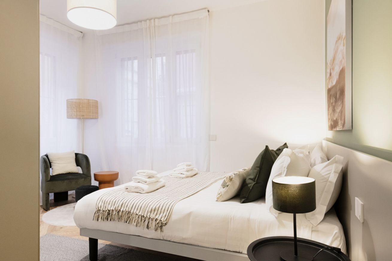 A modern bedroom with a bed, bedside table, lamp, and a chair.