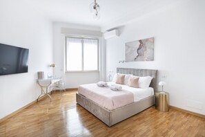 A modern bedroom with a large bed, a desk, and a TV.