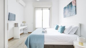 A bedroom with a bed, a desk, a chair, a TV, and a window.