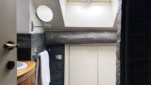 A bathroom with a skylight, a wooden vanity, a round mirror, and a white door.