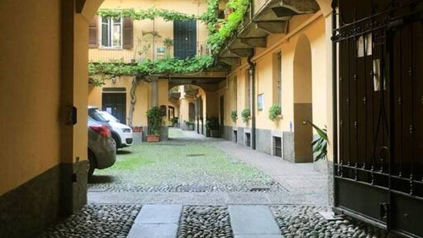 A narrow alleyway with a cobblestone path, a parked car, and a building with a black gate.