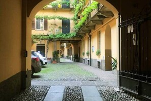 A narrow alleyway with a cobblestone path, a parked car, and a building with a black gate. - Easylife - Enchanting duplex on the rooftops in the heart of the Navigli (Milano)
