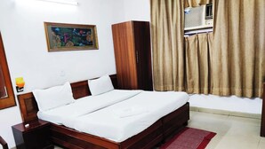 A hotel room with a wooden bed, a nightstand, a red chair, a wooden wardrobe, a painting on the wall, and a window with curtains.