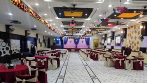 A banquet hall with rows of round tables, each with a red tablecloth and white chair covers. The floor has a patterned tile design.