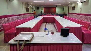 Un salón de conferencias con una larga mesa, sillas rosadas y un mantel blanco.