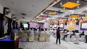 A conference room with rows of white chairs, a stage with a podium, and a large screen.