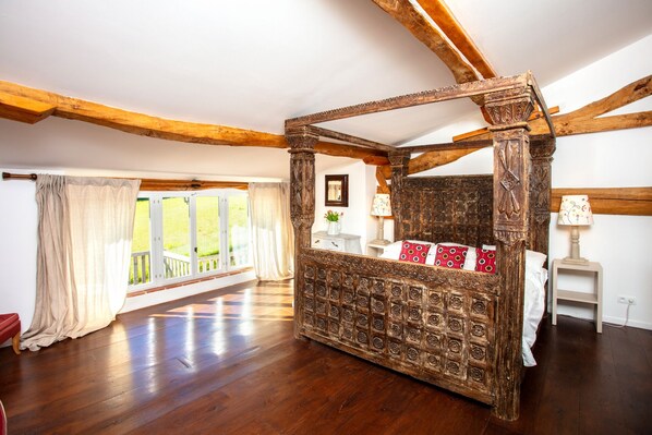 Une chambre dotée d’un grand lit à baldaquin en bois, d’une fenêtre donnant sur l’extérieur et ornée de rideaux, et d’un plancher en bois.