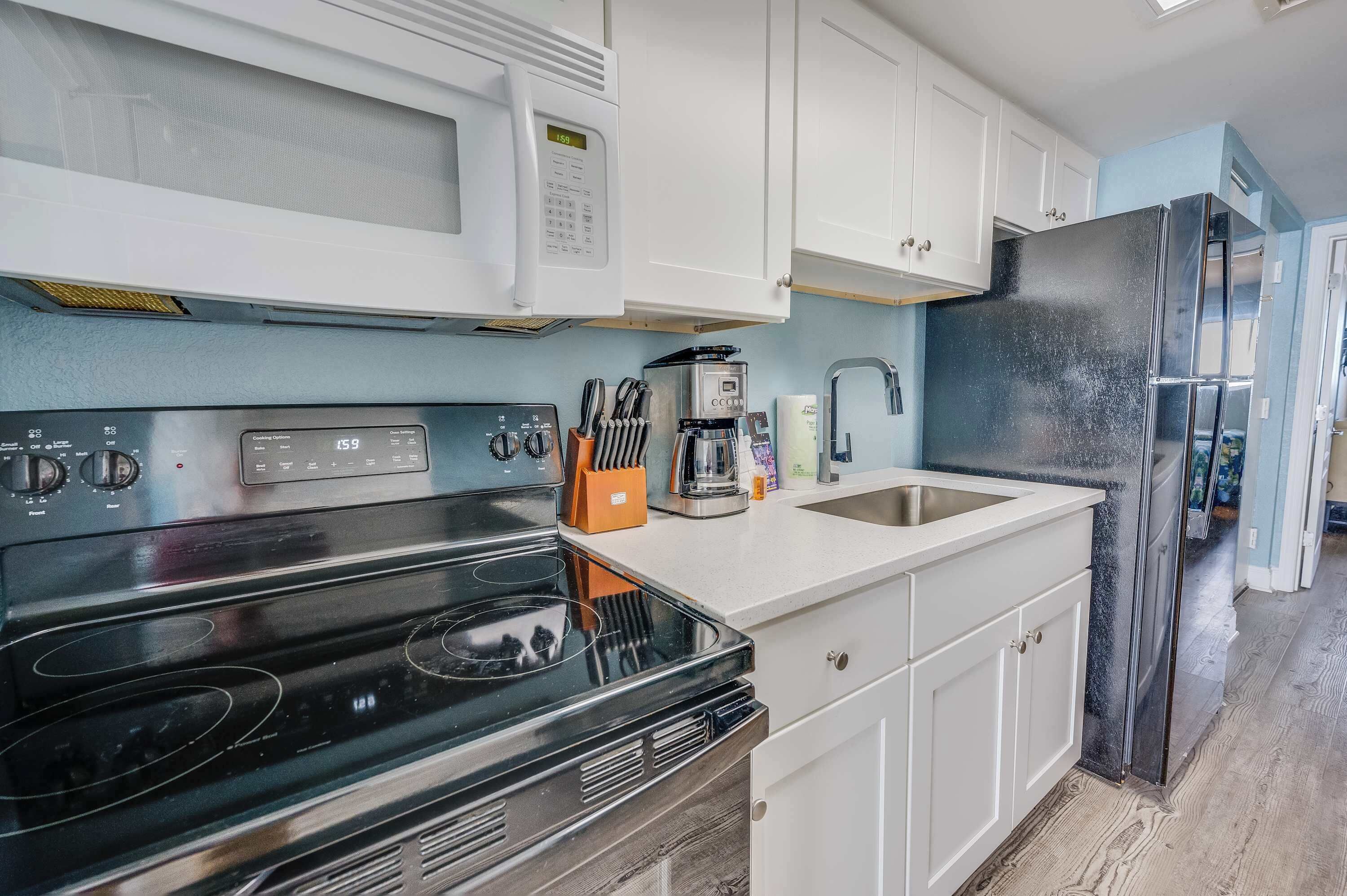 Una cocina moderna con gabinetes blancos, una estufa negra, un microondas, una cafetera y un refrigerador.