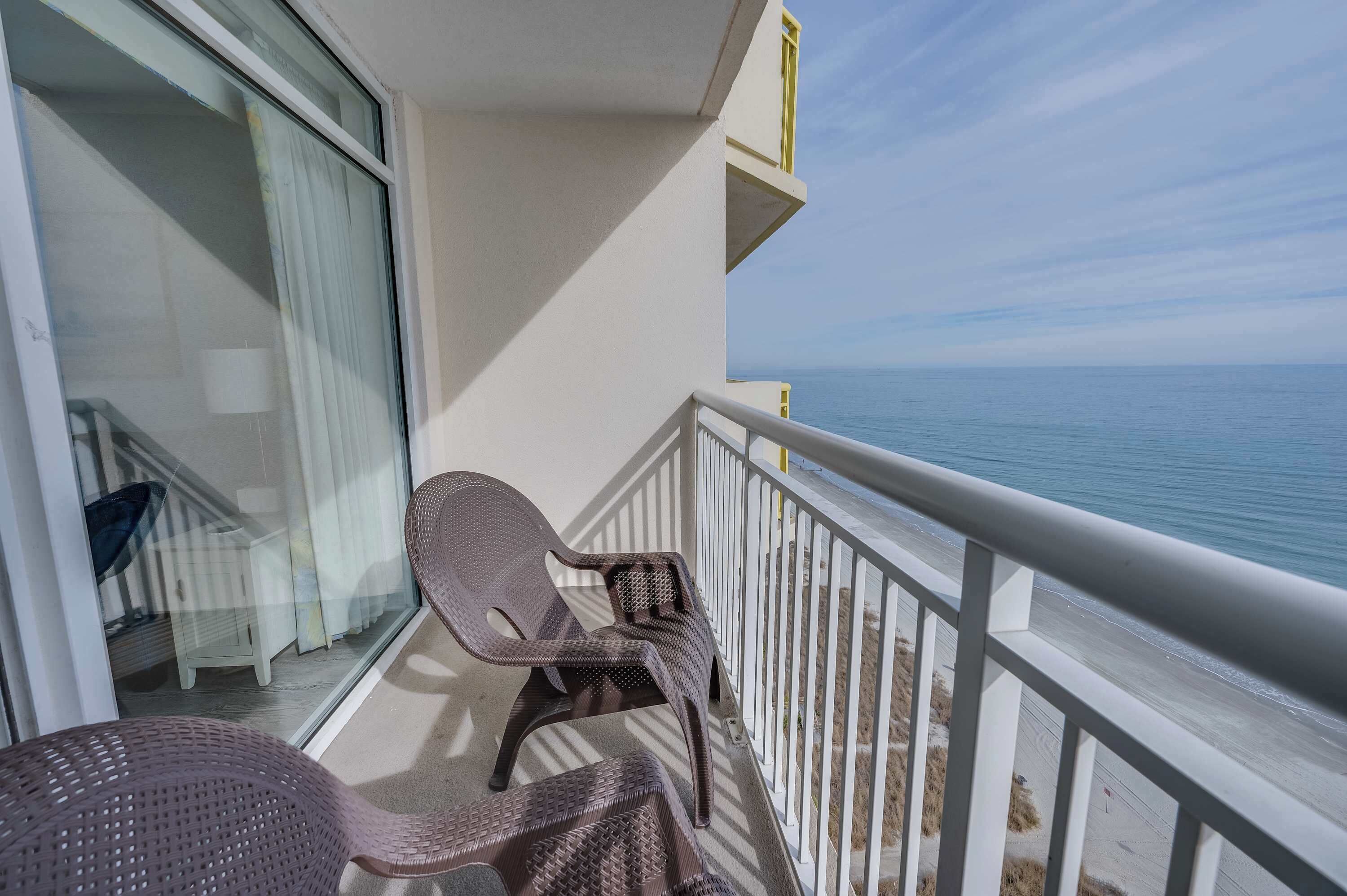 A balcony with two wicker chairs and a glass door leading to a staircase.