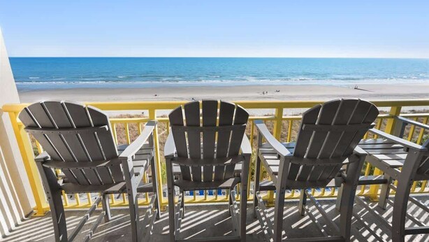 Un balcone con tre poltrone Adirondack rivolto verso una spiaggia.
