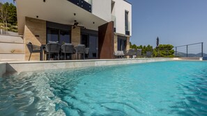 Een modern gebouw met een zwembad, terras en helder uitzicht op zee.