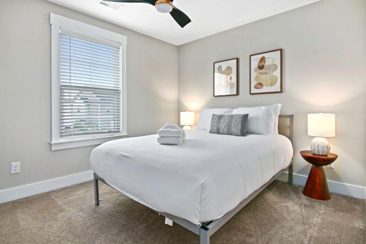 Une chambre à coucher avec un lit, deux lampes de chevet, un ventilateur de plafond et une fenêtre avec des stores.