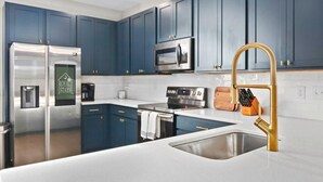A modern kitchen with blue cabinets, stainless steel appliances, and a gold faucet.