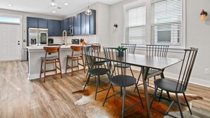 A modern kitchen with dark blue cabinets, a white countertop, and a dining area with a large table and chairs.