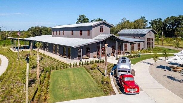 A modern building with a covered outdoor area, a red vintage car, and a silver airplane parked in front.