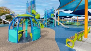A playground with various play structures, including slides and climbing areas, and a shaded seating area.